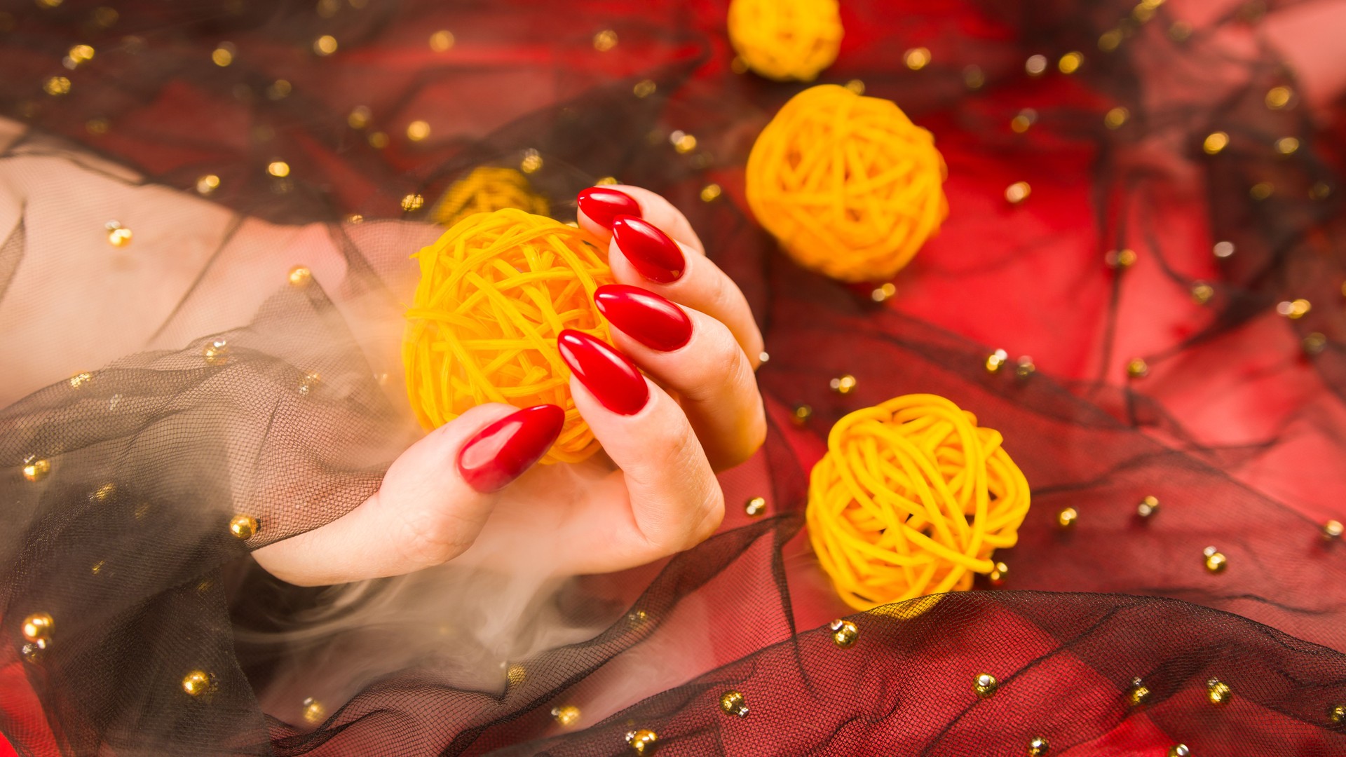 Anonymous female with red manicure with decorative wicker balls on red background