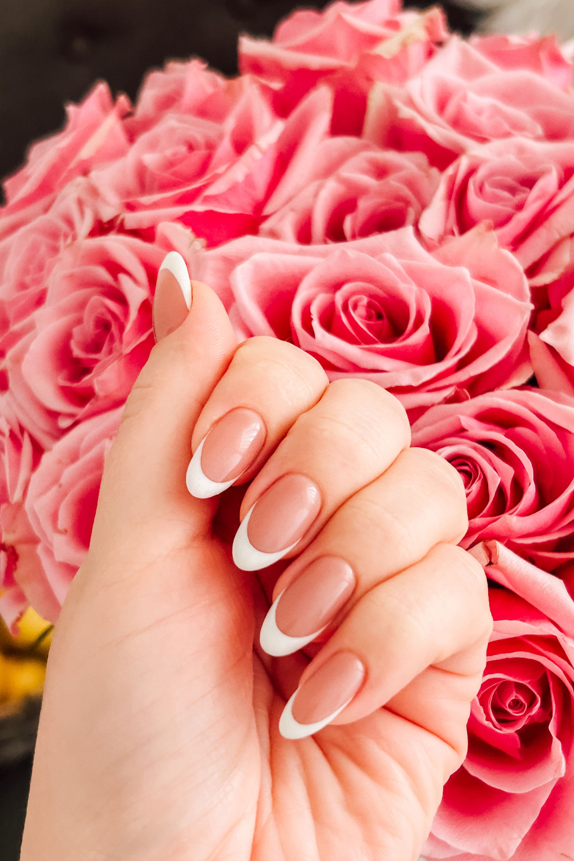 Beautiful hand with French manicure nails holding a bouquet of pink roses at a floral event